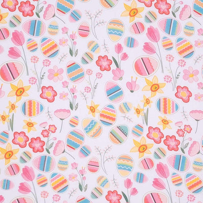 Colourful easter eggs and pink spring flowers and daffodils are printed on a white, 100% cotton fabric