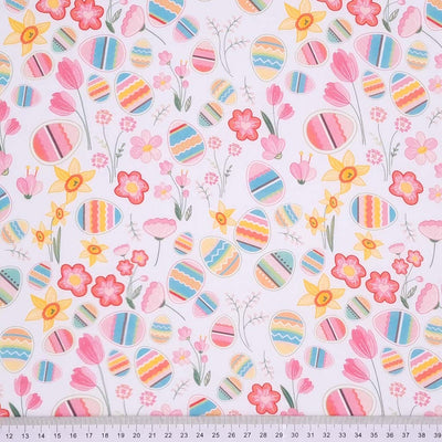 Colourful easter eggs and pink spring flowers and daffodils are printed on a white, 100% cotton fabric with a cm ruler at the bottom