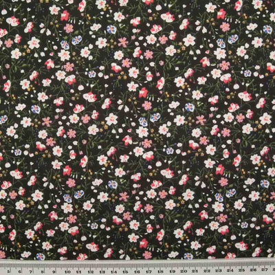 White, pink and blue ditsy flowers are printed on a black polycotton fabric with a ruler at the bottom for size perspective