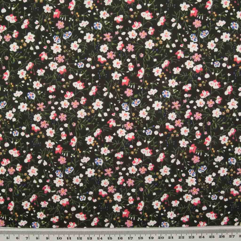 White, pink and blue ditsy flowers are printed on a black polycotton fabric with a ruler at the bottom for size perspective