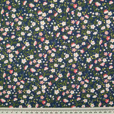 White, pink and blue ditsy flowers are printed on a navy polycotton fabric with a ruler at the bottom for size perspective