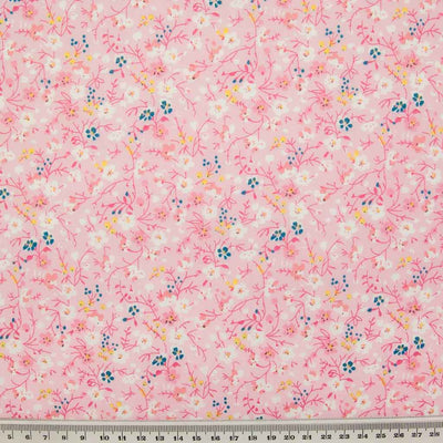 White, pink and blue ditsy flowers are printed on a pink polycotton fabric with a ruler at the bottom for size perspective