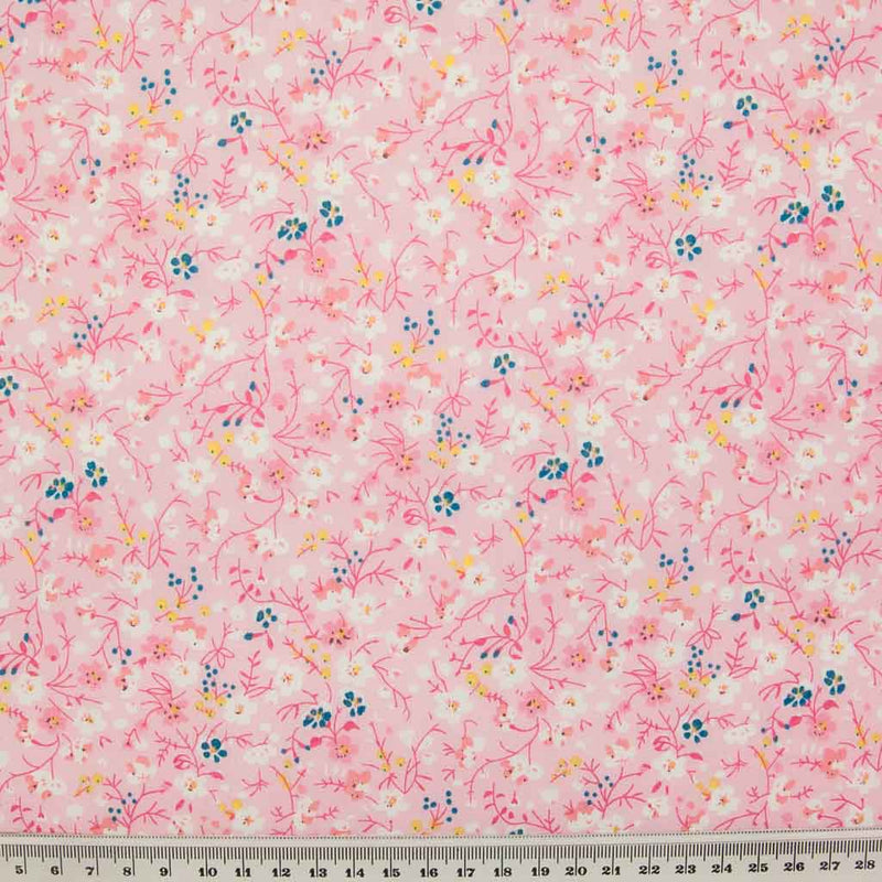 White, pink and blue ditsy flowers are printed on a pink polycotton fabric with a ruler at the bottom for size perspective