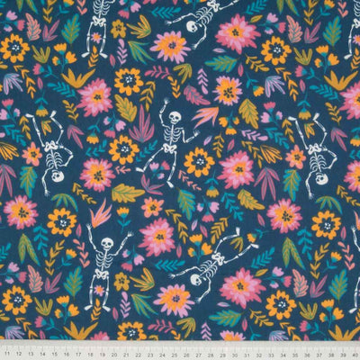 Skeletons dance on a bed of brightly coloured flowers, printed on a blue halloween polycotton fabric with a cm ruler at the bottom