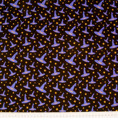 Jaunty purple witches'  hats printed on a black polycotton fabric with a cm ruler at the bottom