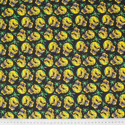 Yellow screaming skulls and green paint splats printed on a black halloween polycotton fabric with a cm ruler at the bottom