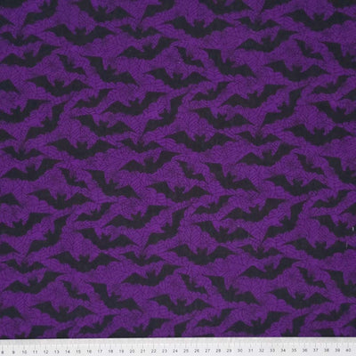 Flying black bats printed on a dark purple polycotton fabric with a cm ruler at the bottom