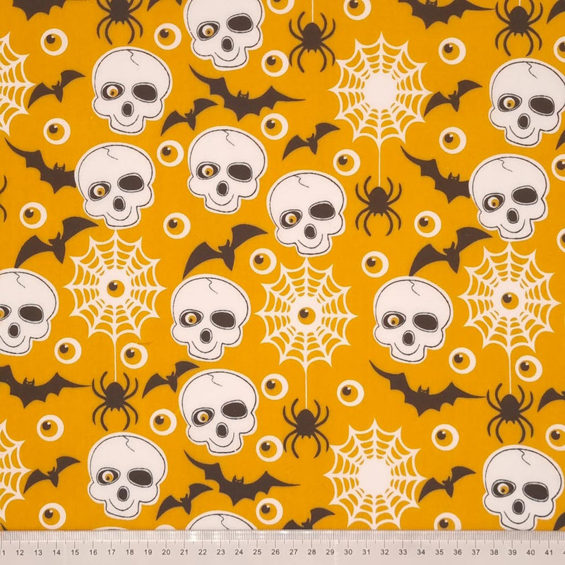 Skulls, eyeballs and bats printed on an orange halloween polycotton fabric with a cm ruler at the bottom