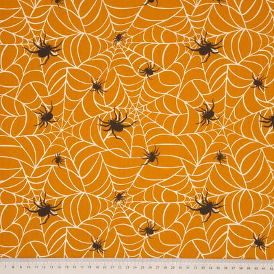 Hairy spiders guarding their webs are printed on an orange polycotton fabric with a cm ruler at the bottom