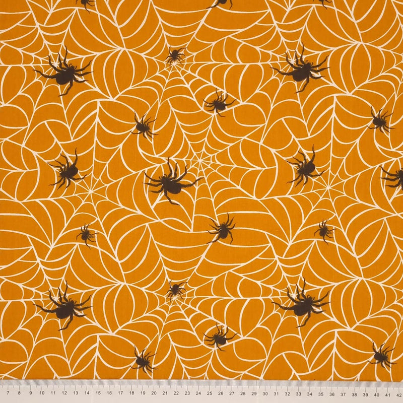 Hairy spiders guarding their webs are printed on an orange polycotton fabric with a cm ruler at the bottom