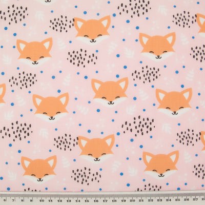 Smiling fox faces are printed on a baby pink polycotton fabric with a ruler at the bottom for size perspective