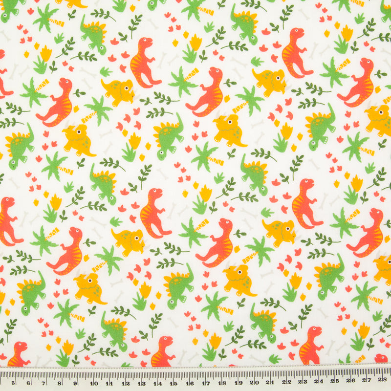 Orange and green dinosaurs are printed on a fat quarter of white polycotton fabric pictured with a ruler at the bottom for size perspective