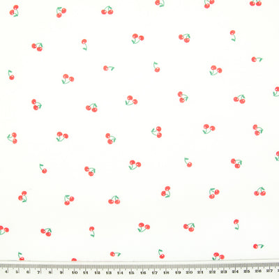 Ditsy red cherries are printed on a white polycotton fabric with a cm ruler