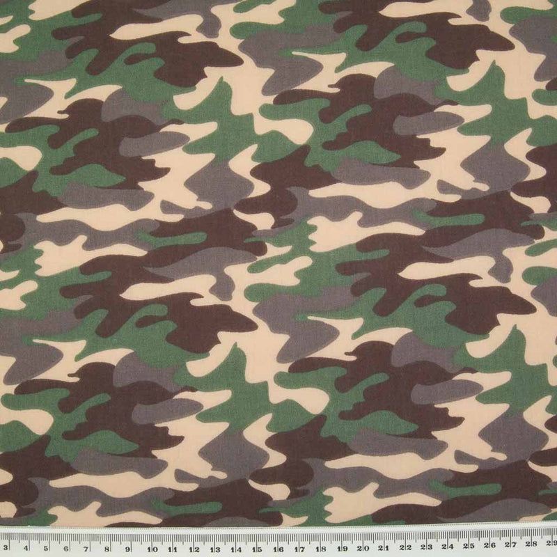 A camouflage design in beige, brown and khaki on a polycotton fabric with a ruler for size perspective