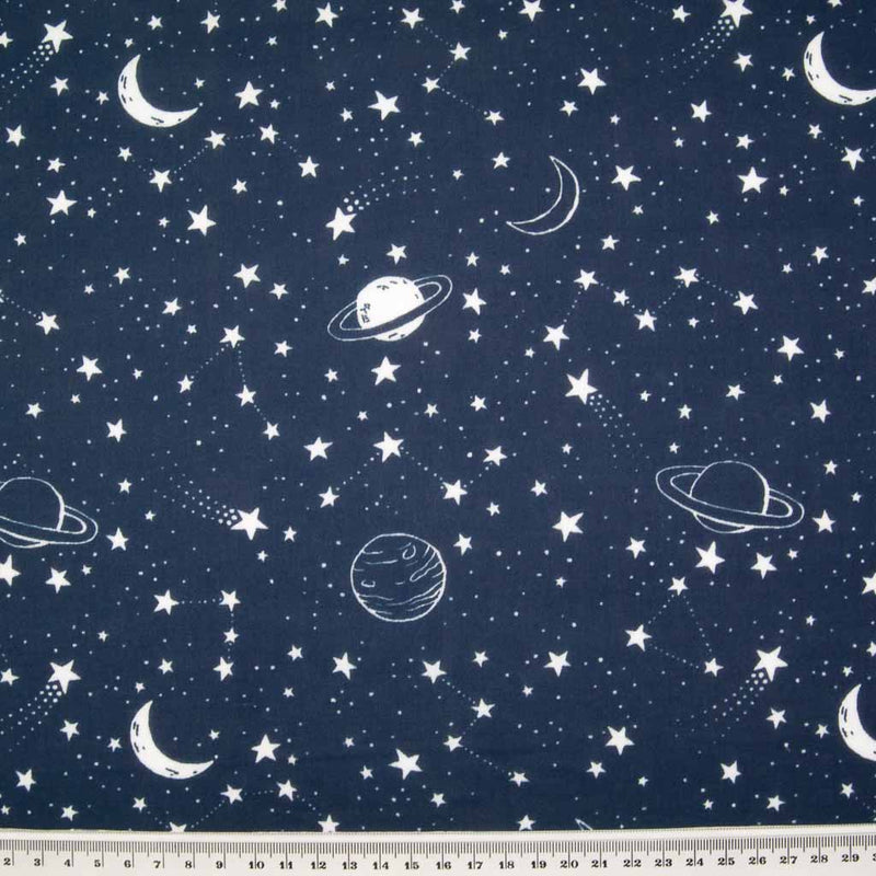 White stars, planets and moons are printed on a navy blue polycotton fabric with a ruler at the bottom for size perspective