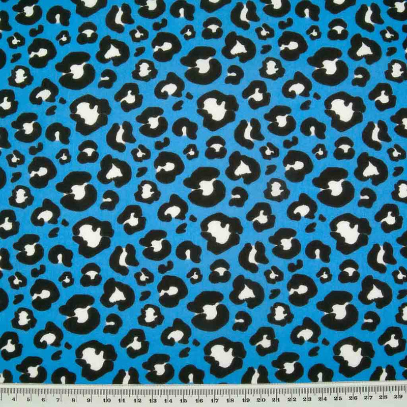 White and black leopard spots printed on a bright blue polycotton fabric with a ruler for size perspective