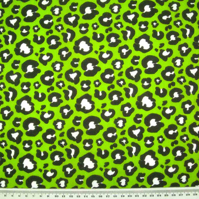 Striking white and black leopard spots printed on a green polycotton fabric with a ruler for size perspective