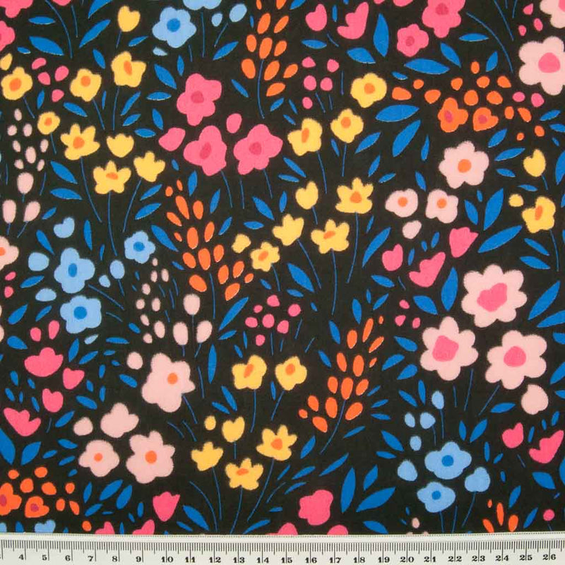 Primary coloured flowers printed on a black polycotton fabric with a cm ruler at the bottom