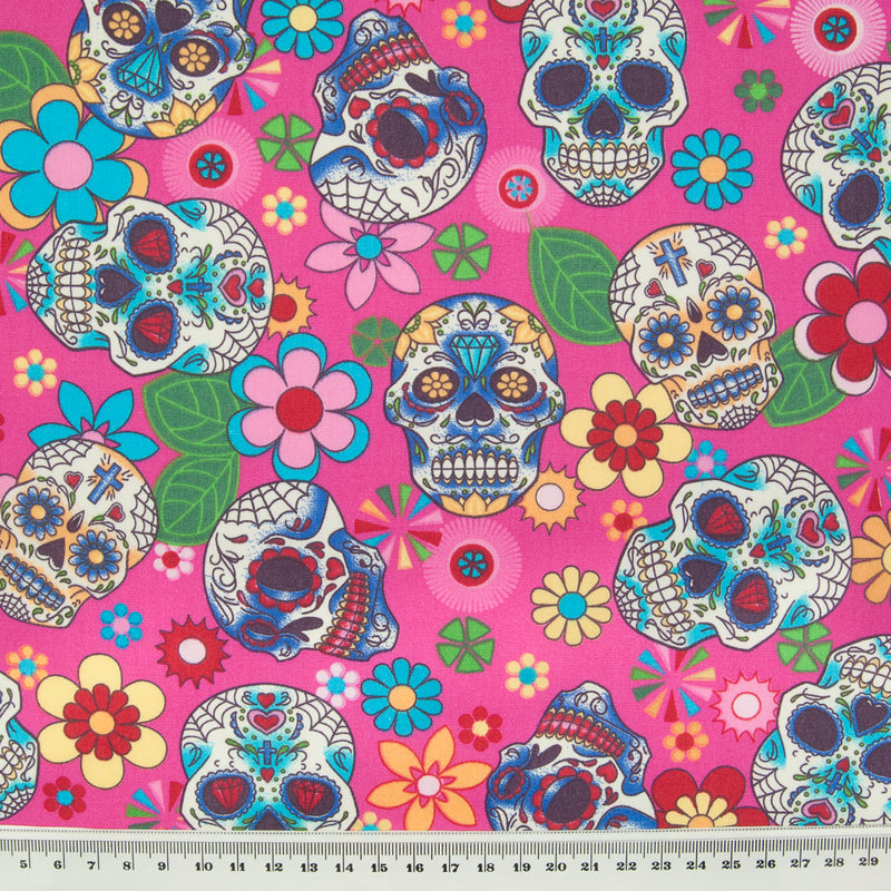 A Rose & Hubble cotton fabric with bright and colourful skulls and flowers printed on a cerise background with ruler for size perspective