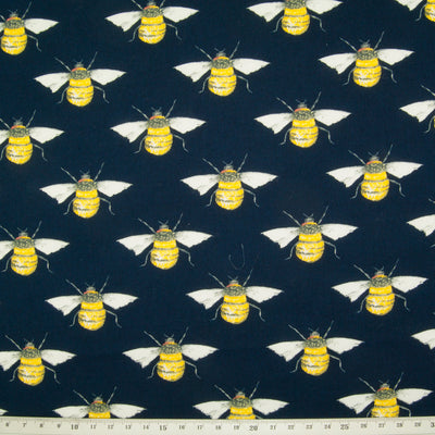 Large black and yellow bees in a geometric pattern on a flat piece of navy blue cotton poplin fabric with a ruler at the bottom for size perspective