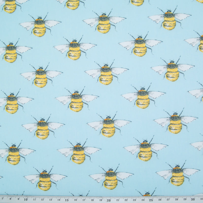 Large black and yellow bees in a geometric pattern on a flat piece of sky blue cotton poplin fabric with a ruler at the bottom for size perspective