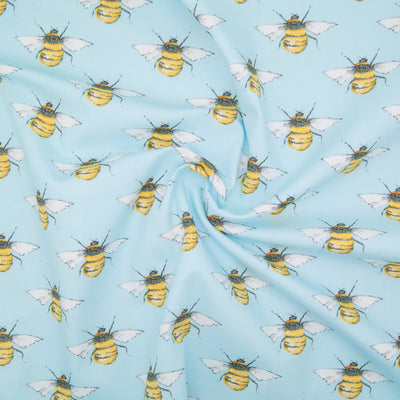 Large black and yellow bees in a geometric pattern on a flat piece of sky blue cotton poplin fabric in a swirl for drape perspective.