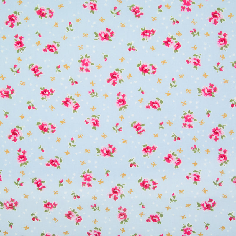 Small, single scattered cerise roses with tiny white hearts and ochre bows printed on a sky blue Rose and Hubble cotton fabric pictured flat