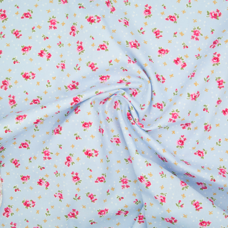 Rose and Hubble ditsy Alice rose on sky blue  cotton fabric pictured in a swirl for drape perspective