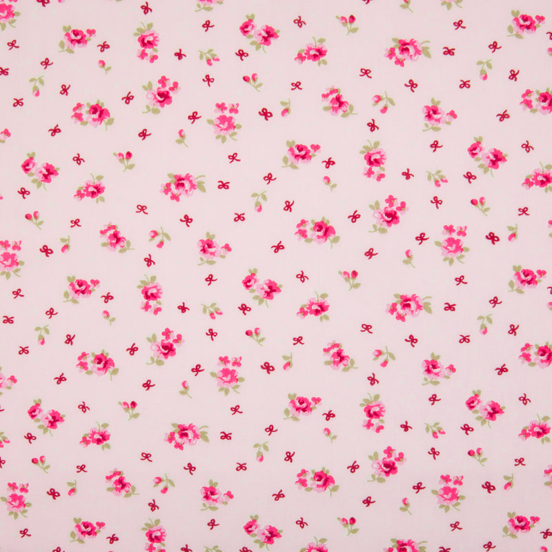 Small, single scattered cerise roses with tiny white hearts and ochre bows printed on a pink Rose and Hubble cotton fabric pictured flat