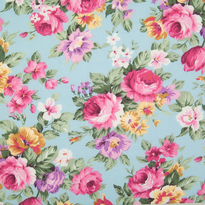 Bunches of large pink roses with lilac and yellow flowers on a sky blue Rose and Hubble cotton poplin fabric pictured flat