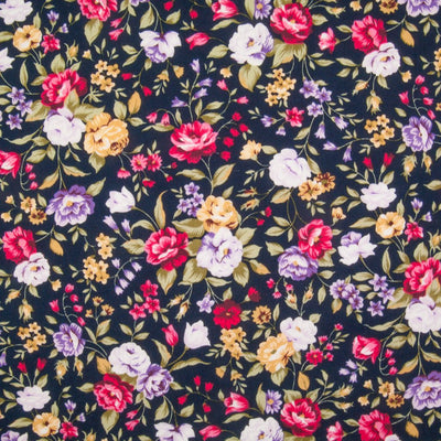 A dense pattern of cerise and lilac flowers in vivid colours printed on a navy Rose & Hubble cotton poplin fabric pictured flat