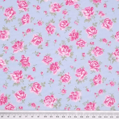 Dusky pink roses are printed on a sky blue cotton poplin fabric by Rose & Hubble with a cm ruler