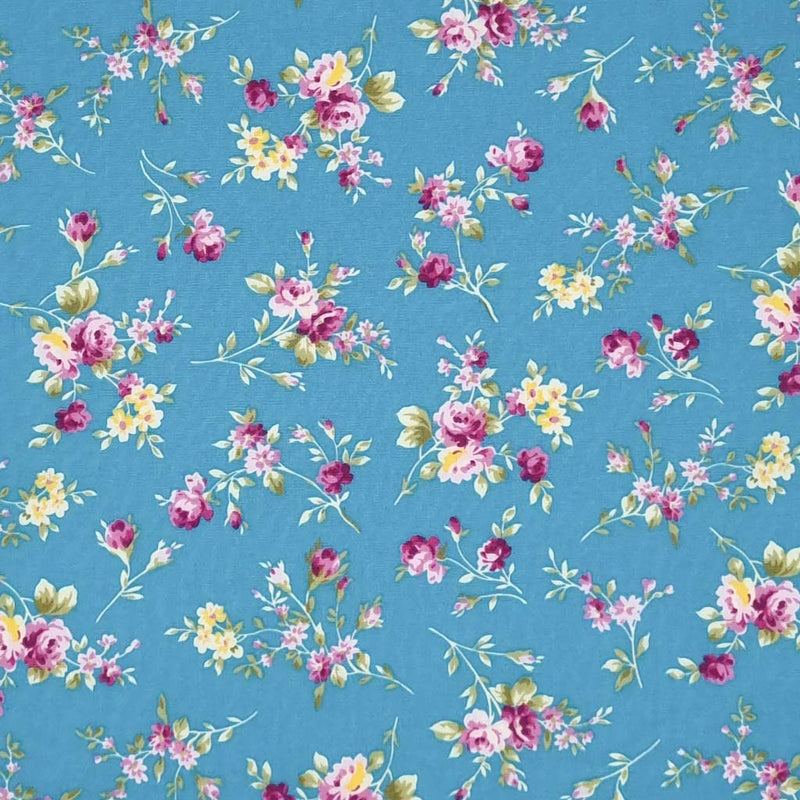 Bunches of cerise roses are printed on a copen blue cotton poplin fabric by Rose & Hubble