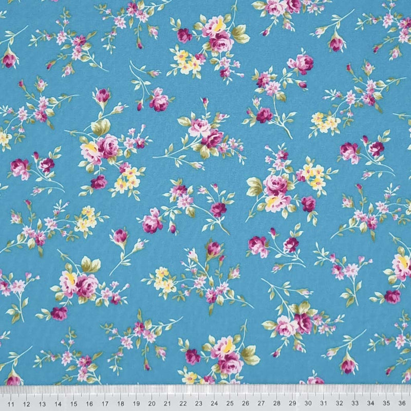 Bunches of cerise roses are printed on a copen blue cotton poplin fabric by Rose & Hubble with a cm ruler