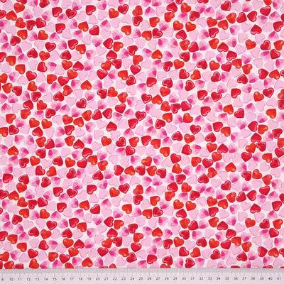 Small pink and red hearts are printed on a white, 100% cotton poplin by Rose & Hubble with a cm ruler at the bottom
