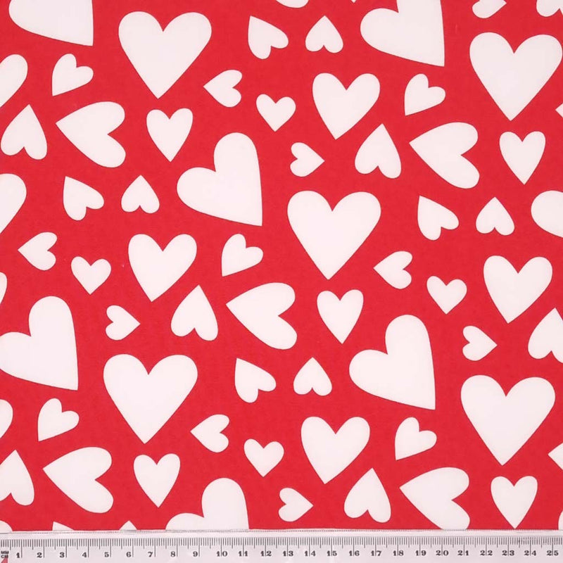 Multi sized white hearts printed on a red cotton poplin fabric with a cm ruler