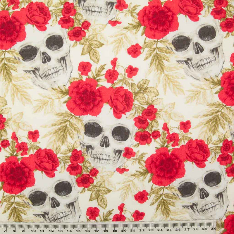 White skulls appear through a bed of red roses all printed on a n ivory 100% cotton poplin fabric by Rose and Hubble with a ruler for size perspective