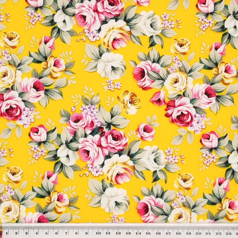 Sprays of pink roses with sage green leaves printed on a yellow, lightweight cotton poplin fabric with a cm ruler
