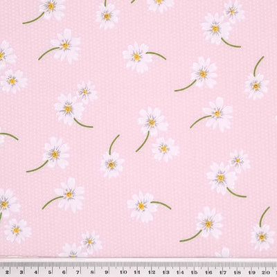 White daisies in a scattered pattern are printed on a pink polycotton fabric with tiny white spots with a cm ruler