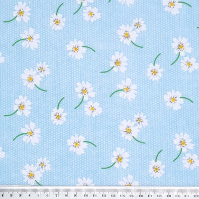 White daisies in a scattered pattern are printed on a sky blue polycotton fabric with tiny white spots. with a cm ruler
