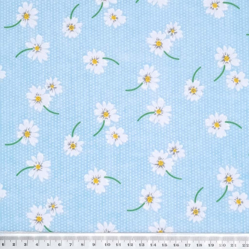 White daisies in a scattered pattern are printed on a sky blue polycotton fabric with tiny white spots. with a cm ruler