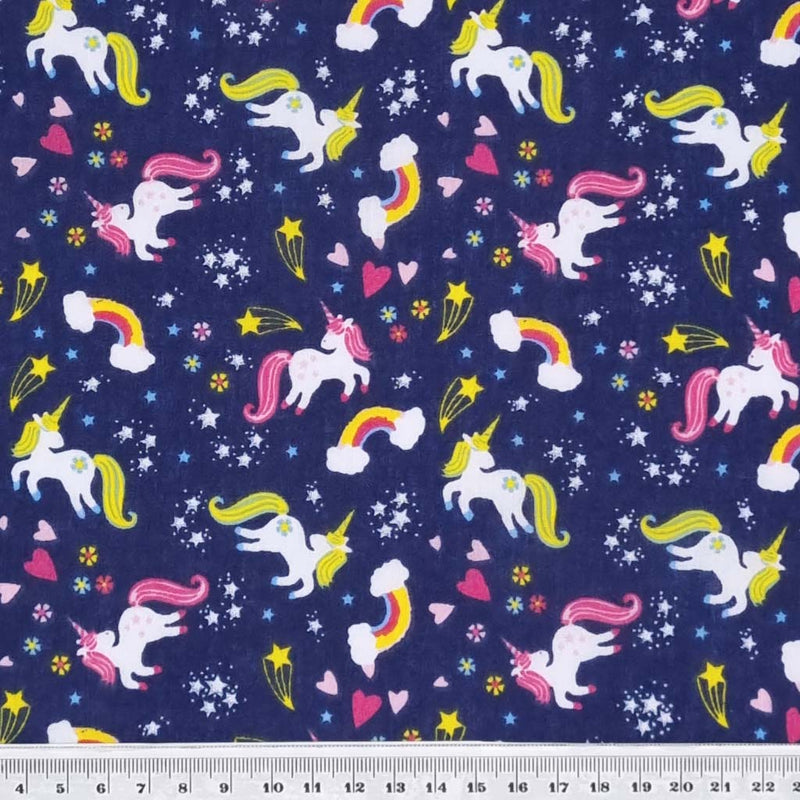 Unicorns, rainbows and stars are printed on a navy polycotton fabric with a cm ruler at the bottom