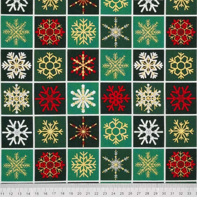 Printed gold, red and white metallic snowflakes are printed on this bottle green checkboard style 100% cotton fabric with a cm ruler at the bottom