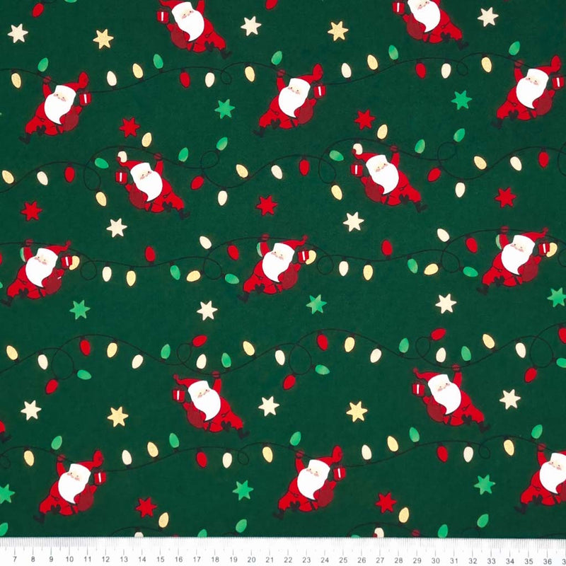 Santa holding strings of fairy lights printed on a green christmas cotton fabric with a cm ruler