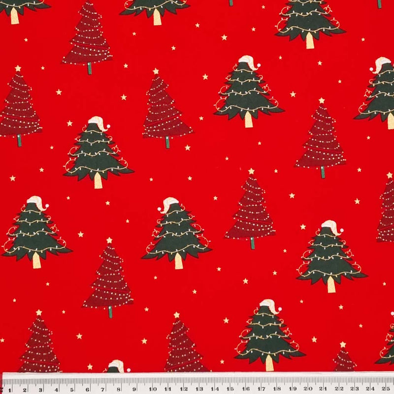 Red and green christmas trees with fairy lights are printed on a red christmas cotton fabric with a cm ruler at the bottom