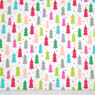 Colourful christmas trees in reds and greens are printed on a white polycotton fabric with a cm ruler at the bottom
