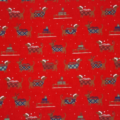 cute dachshund sausage dogs wearing Christmas jumpers and sledges laden with gifts are printed on a red polycotton fabric