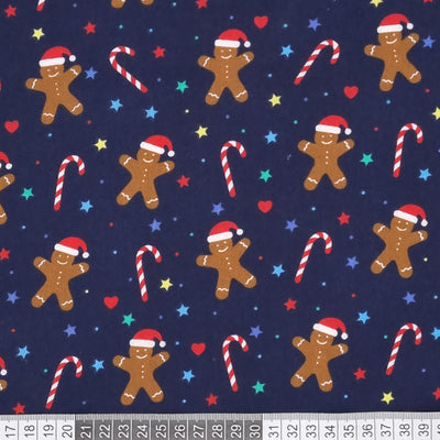 Smiley gingerbread men, hearts, stars and candy canes are printed on a navy polycotton fabric with a cm ruler at the bottom