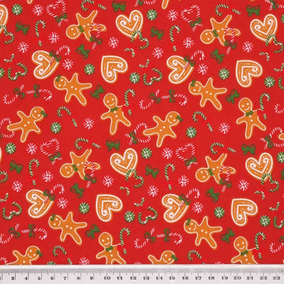 Cute gingerbread men, candy canes and hearts on a red polycotton fabric with a cm ruler