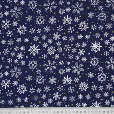 falling snowflakes and gold stars are printed on a navy polycotton fabric with a cm ruler at the bottom